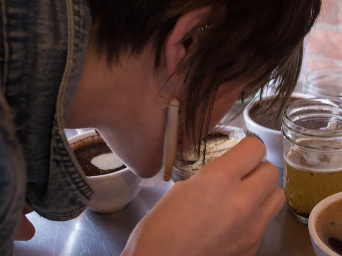 Una catadora acerca la nariz a una cuchara con café, junto a las tazas de la cata