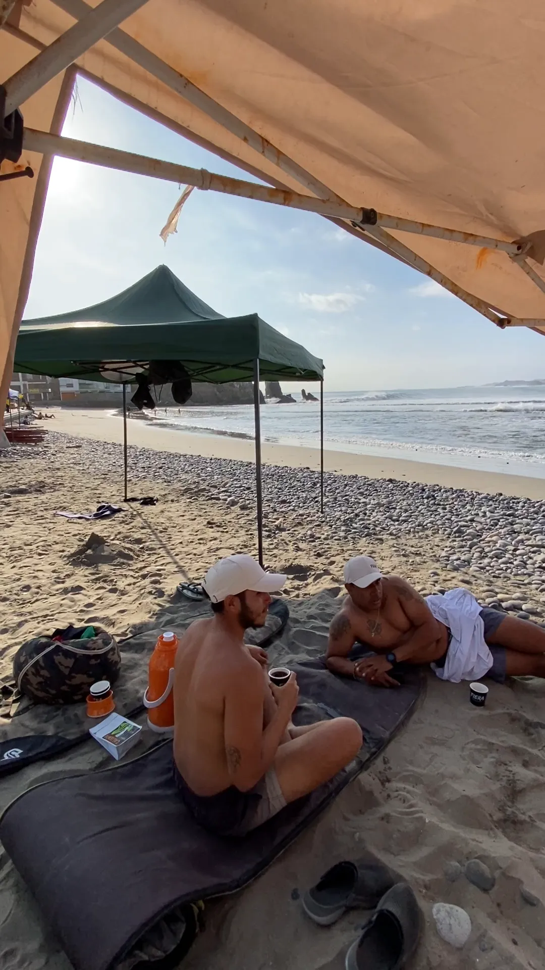 Amigos tomando café bajo el toldo en la playa durante el Surf Day de Caliente Café